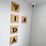 Decoración en pared con letras que forman la palabra "VIDA", hechas de madera con detalles en negro, junto a una cámara de seguridad instalada en la esquina superior.