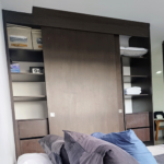 Armario empotrado de madera con puertas corredizas, estantes abiertos que contienen toallas, una caja fuerte y cajas organizadoras, ubicado en una habitación moderna.