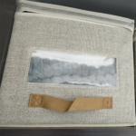 Cobijas de felpa gris almacenadas en una caja organizadora con ventana transparente, ideales para el clima frío.