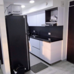 Cocina moderna de diseño integral con muebles blancos, encimeras negras, electrodomésticos como un microondas y una nevera, y accesorios como cafetera y basurero.