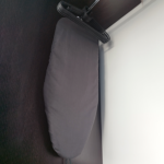 Mesa de planchar plegable con funda oscura colgada junto a un grupo de ganchos plásticos negros en el interior de un armario.