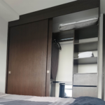 Armario empotrado con puertas corredizas de madera, que contiene una mesa de planchar, ganchos, toallas y almohadas adicionales, ubicado en una habitación moderna.