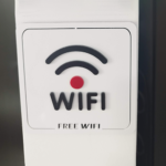 Cartel con el ícono de señal WiFi, un punto rojo y las palabras "WiFi" y "Free WiFi" en un fondo blanco.