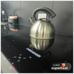 Tetera de acero inoxidable sobre estufa de inducción Challenger en cocina moderna con encimeras negras.