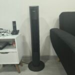 Ventilador de torre negro junto a un sofá y una mesa auxiliar en la sala.